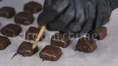 贝克`的手在面包师的纸上用金色条纹装饰巧克力手工糖果。 特写镜头。